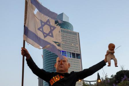 A demonstrator wearing a mask depicting Israeli Prime Minister Benjamin Netanyahu holds a flag and doll during an anti-government protest calling for action to secure the release of Israeli hostages held captive since the October 7, 2023 attacks by Palestinian militants, in front of the Defence Ministry in Tel Aviv on May 31, 2025. (Photo by Jack GUEZ / AFP)